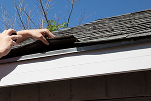 Hand fixing shingles on side of house.